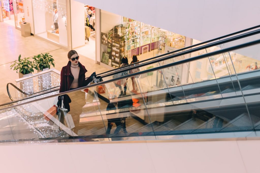 Mulher subindo escada rolante em shopping com sacolas de compra