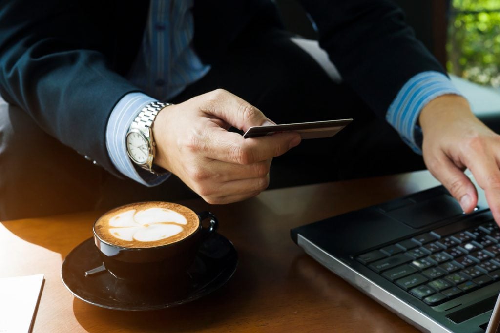 business man drinking coffe using credit card online
