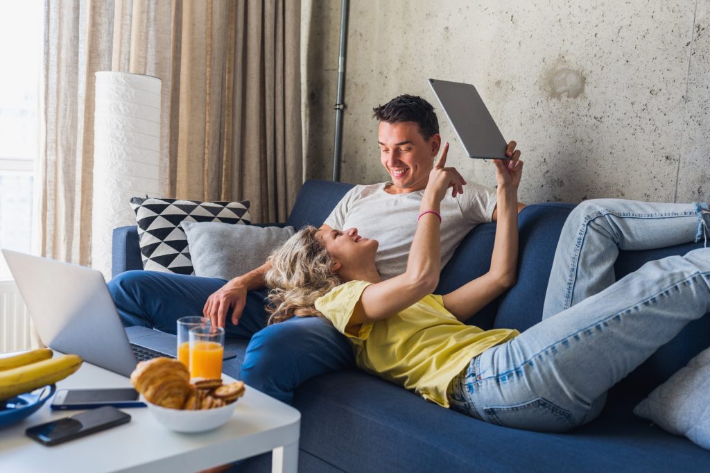 young-couple-sitting-sofa-home-looking-tablet-watching-online