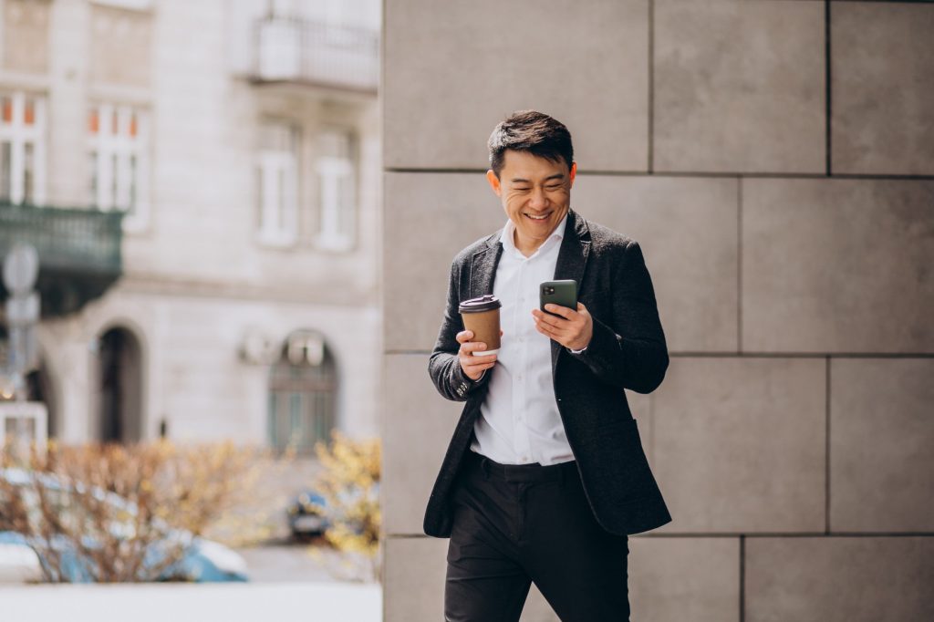 young-handsome-asian-business-man-black-suit-using-phone-drinking-coffee