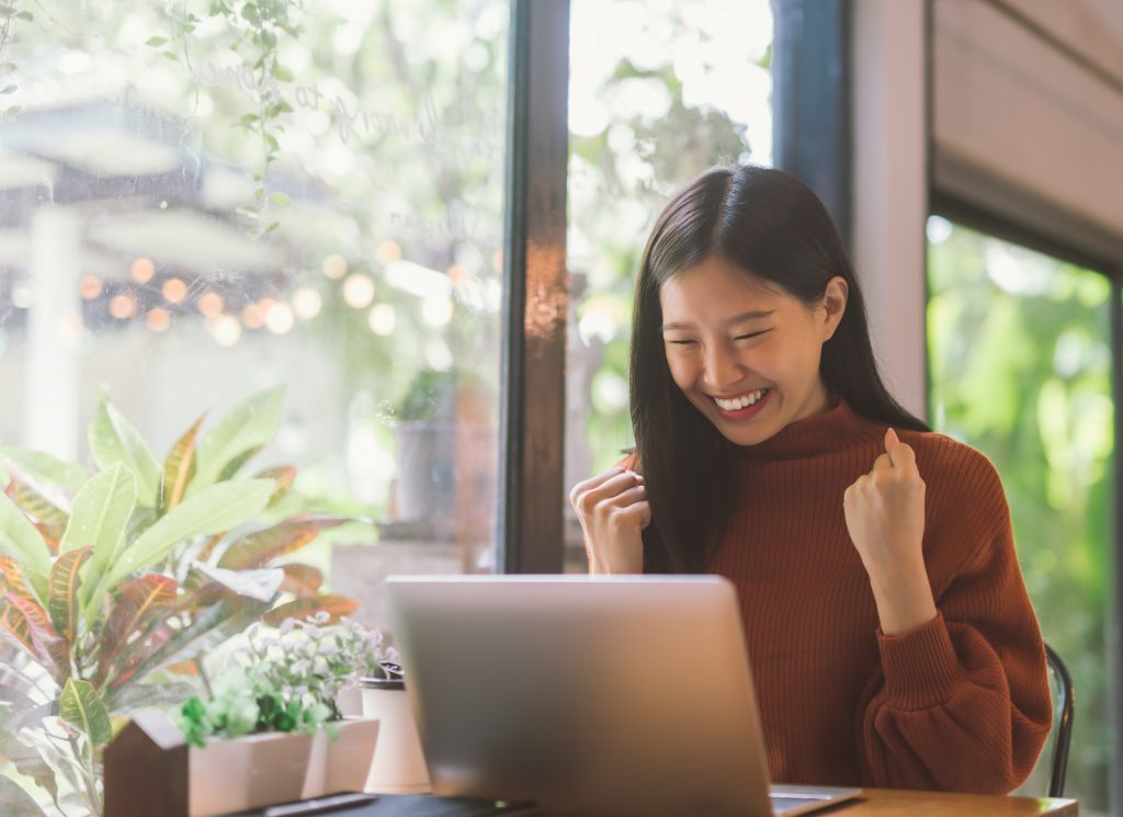 Young Asian woman celebrate success or happy pose with laptop