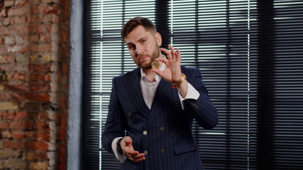 Young attractive successful businessman is holding a bitcoin coin. The concept of successful investment in cryptocurrency