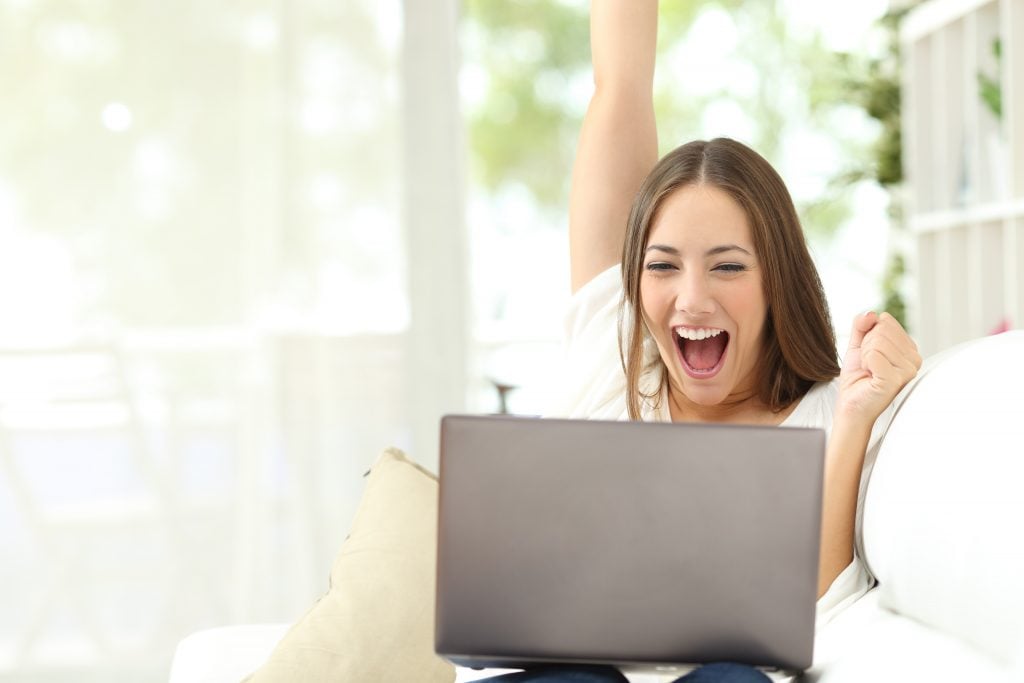 Excited girl celebrating good news on laptop at home