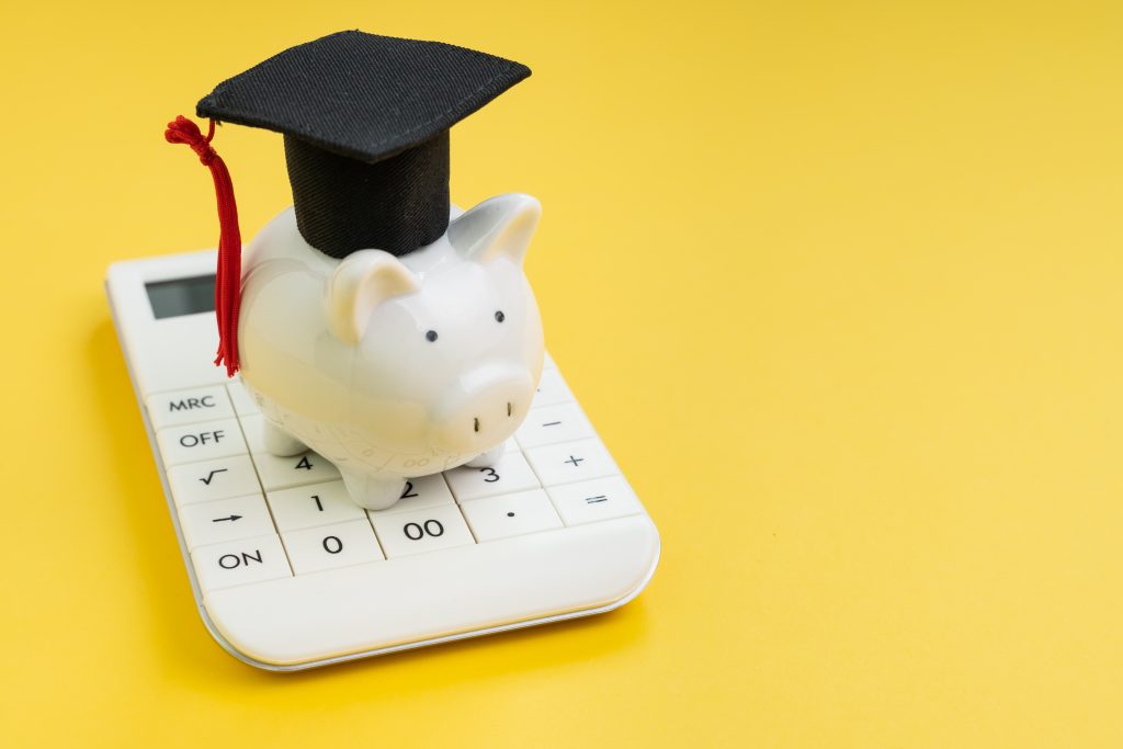 Student loan payment calculation, scholarship or saving for school and education concept, white piggy bank wearing graduation hat on calculator on yellow background with copy space.