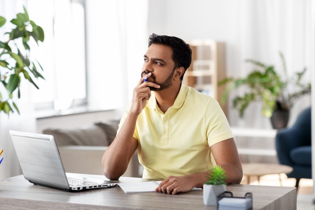 indian man with notebook and laptop at home office