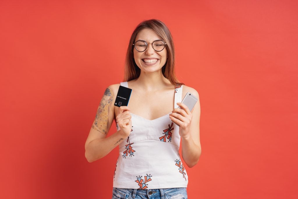 Excited pretty young woman holding phone and credit card in her hands in the studio
