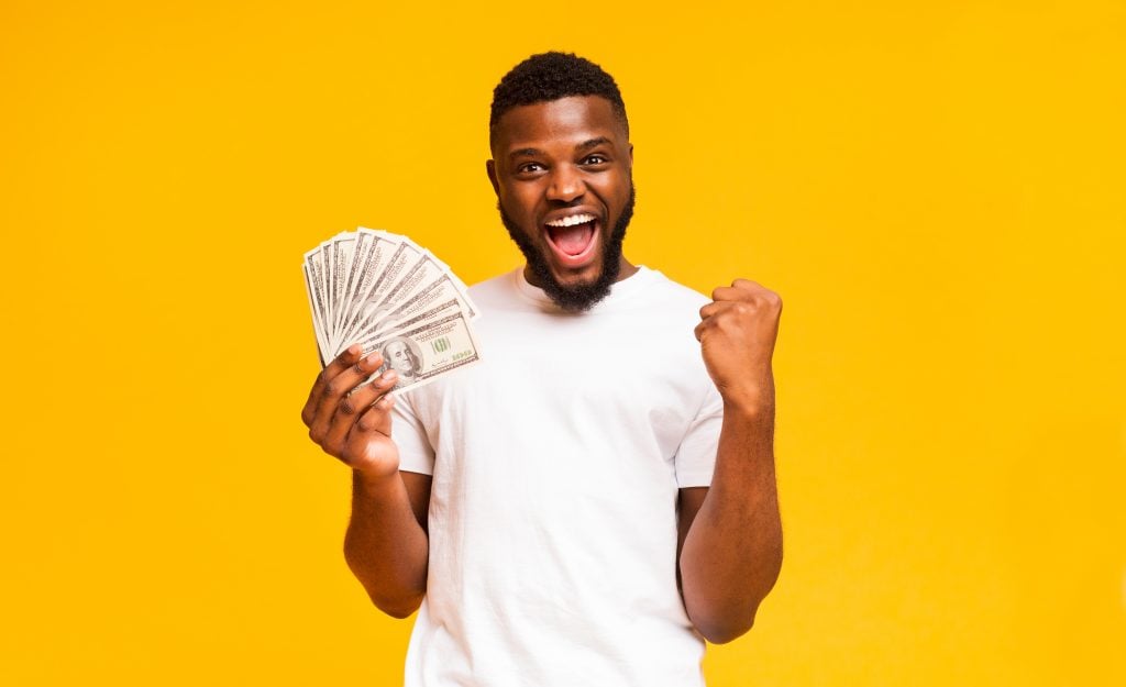 Handsome black guy holding fan of dollars celebrating success