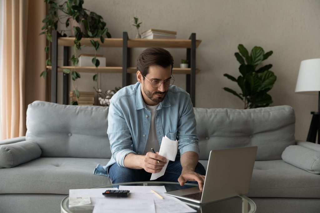 Serious millennial male focused on paying utility bills using laptop