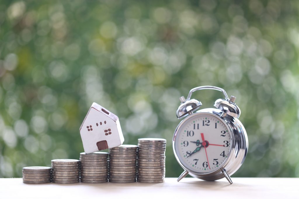 Model house on stack of coins money and alarm clock on natural g