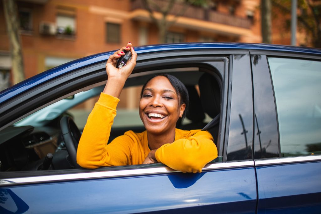 Happy black woman sitting in her new car and showing keys