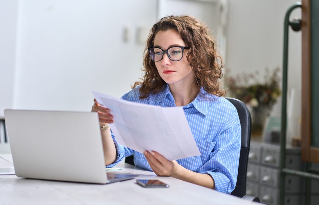 Young business woman manager holding documents working in office with laptop.