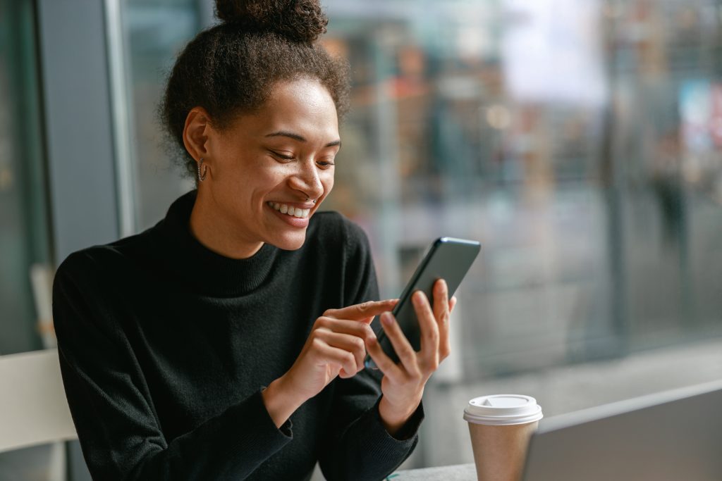 Cheerful woman holding phone during working in cafe near window. Distance work concept