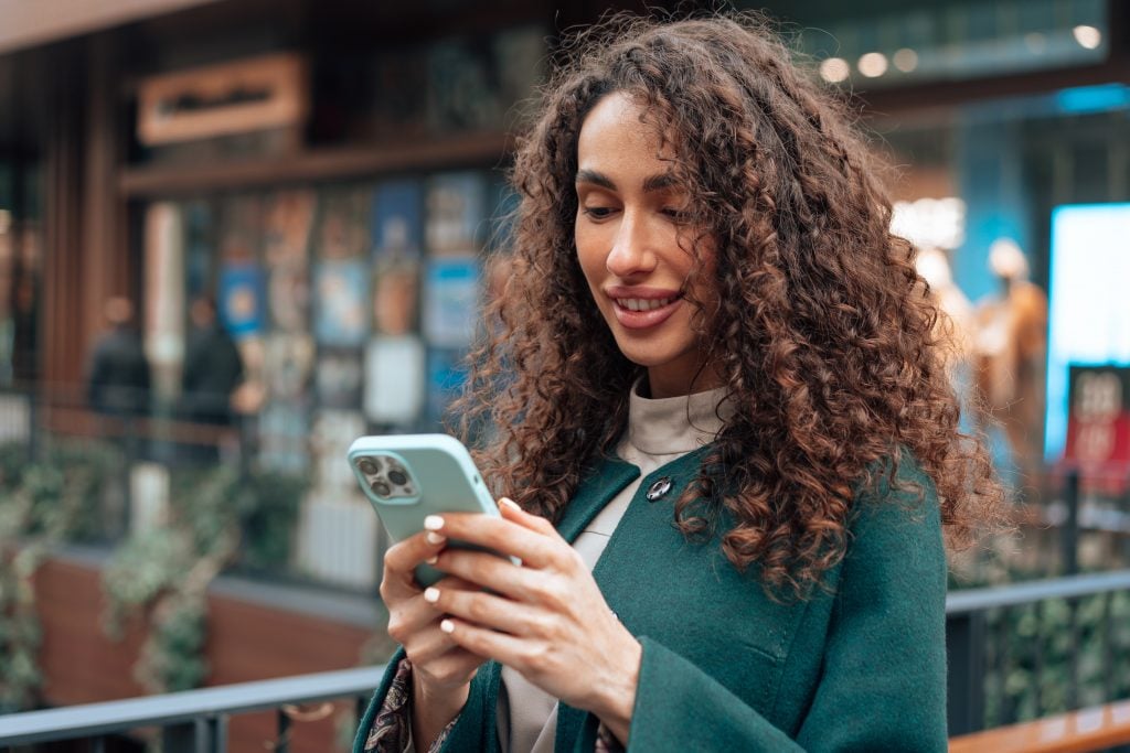 Beautiful young woman in green coat using her cellphone in the city