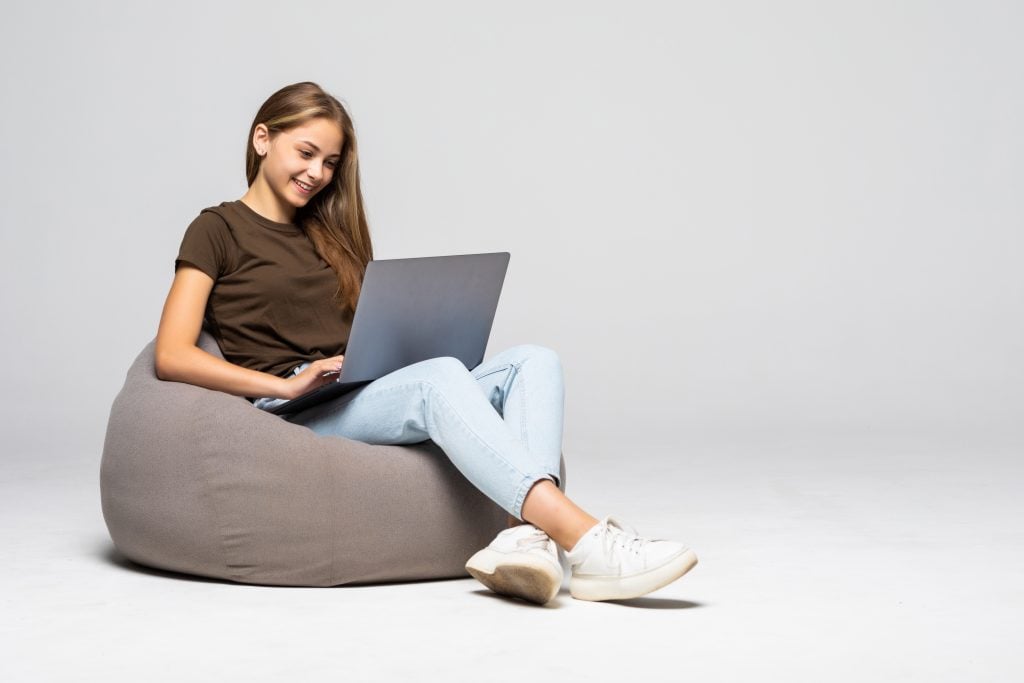 Happy young woman sitting on the floor using laptop on gray background