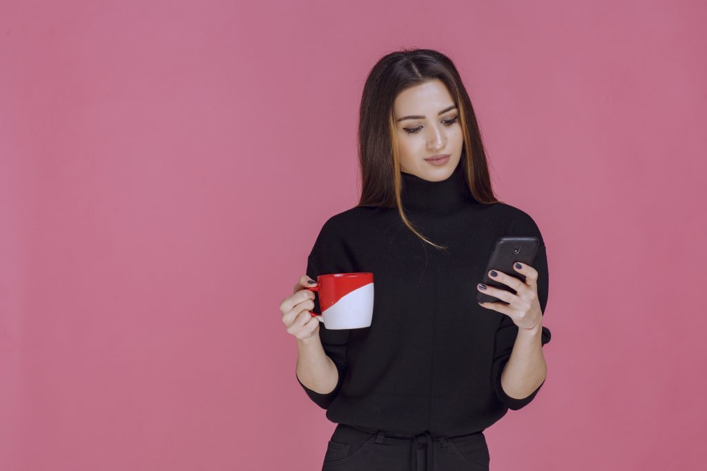 Woman in black shirt holding a coffee cup and talking to the phone