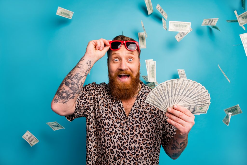 Photo of excited macho guy hold fan usa bucks good mood money luxury rich person dollars fall income lottery cashback wear leopard shirt sun specs isolated blue background