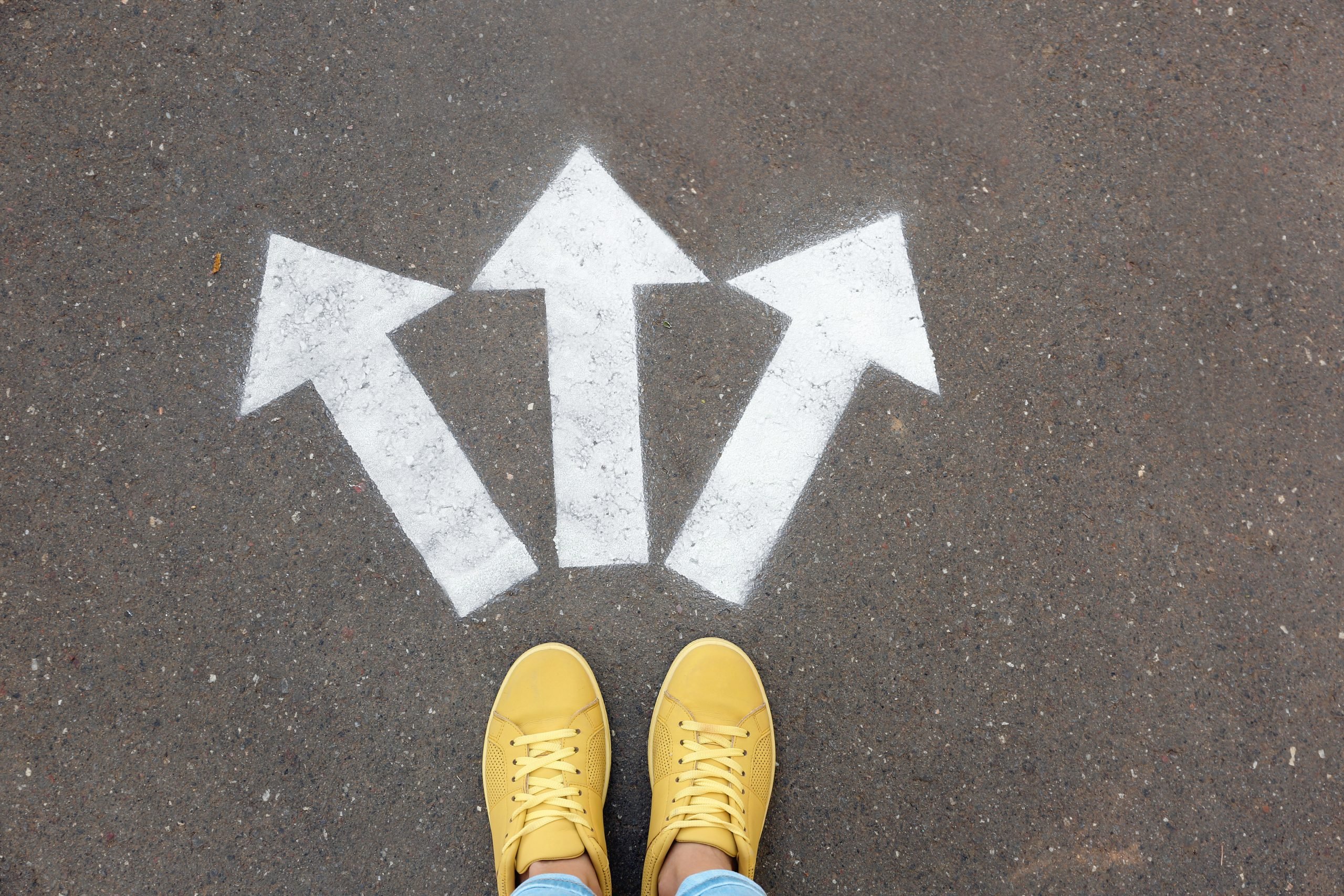 Woman standing near arrows on asphalt, top view. Choice concept