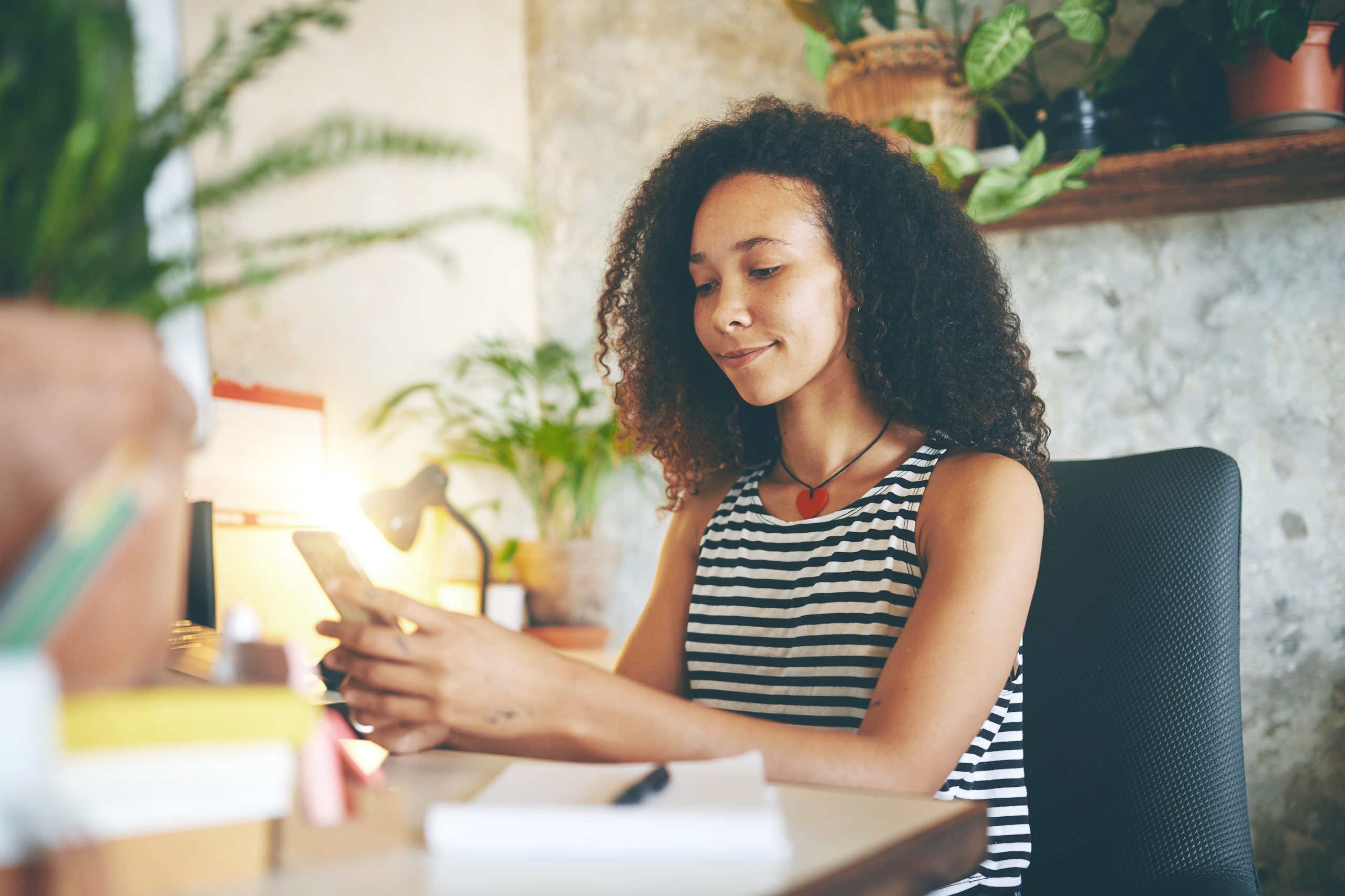 Shot of a young woman sitting alone and using her cellphone to work from home stock photo