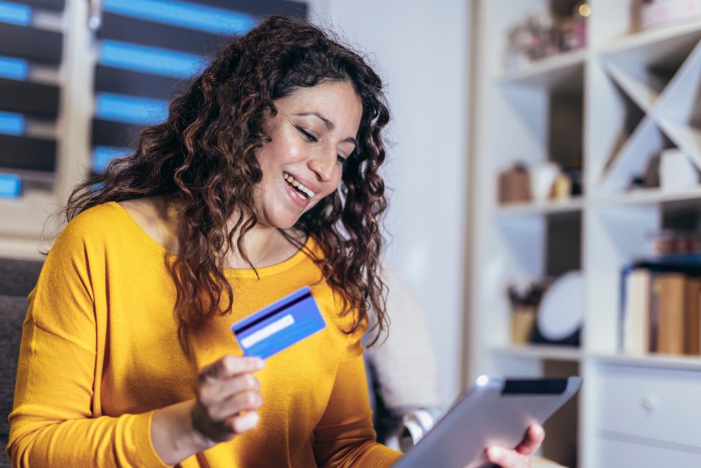 Woman sitting on couch in living room, holding credit card and d