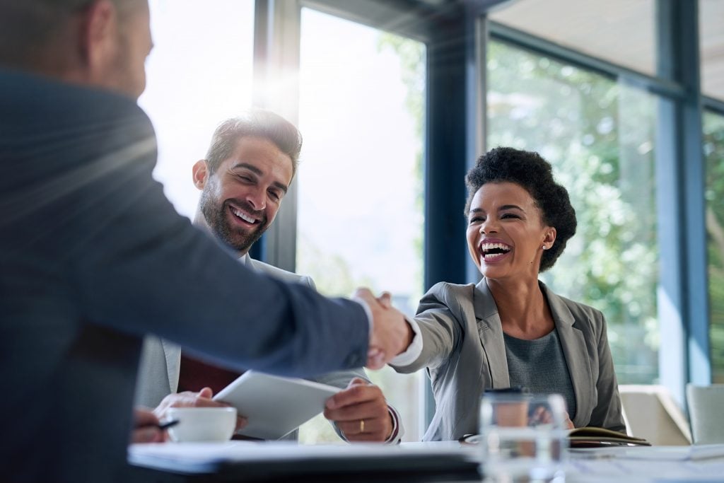 Meeting, partnership and business people shaking hands in the office for a deal, collaboration or onboarding. Diversity, professional and employees with handshake for agreement, welcome or greeting.