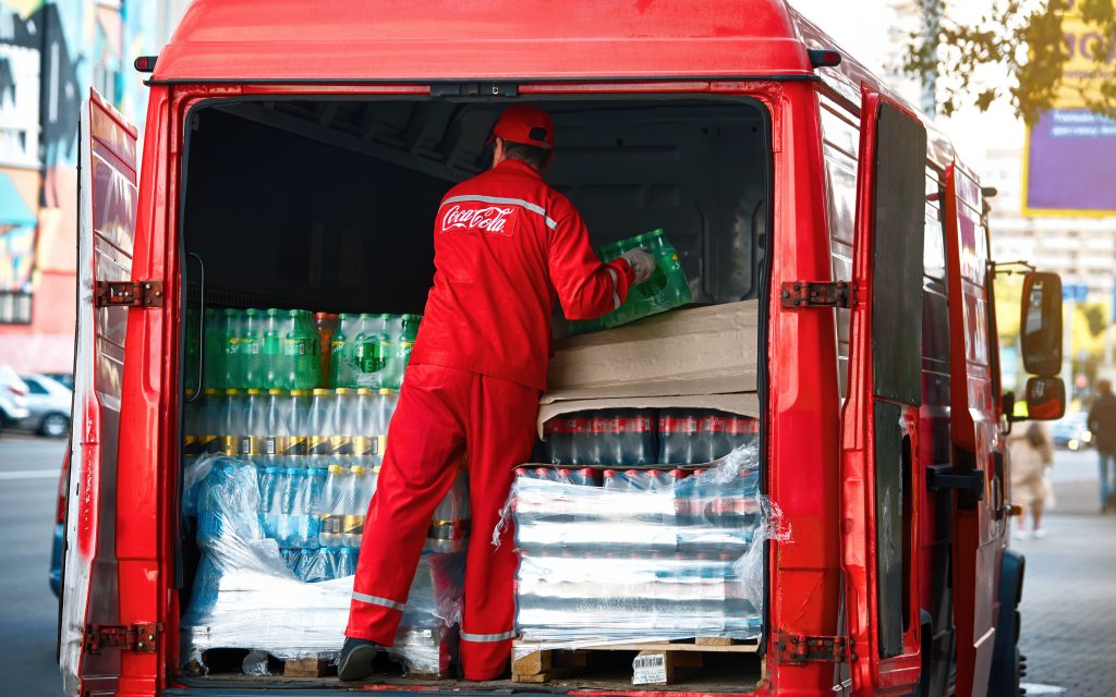 Delivery driver unload car with boxes of beverage, restaurant delivery. Van with Coca-cola drinks.