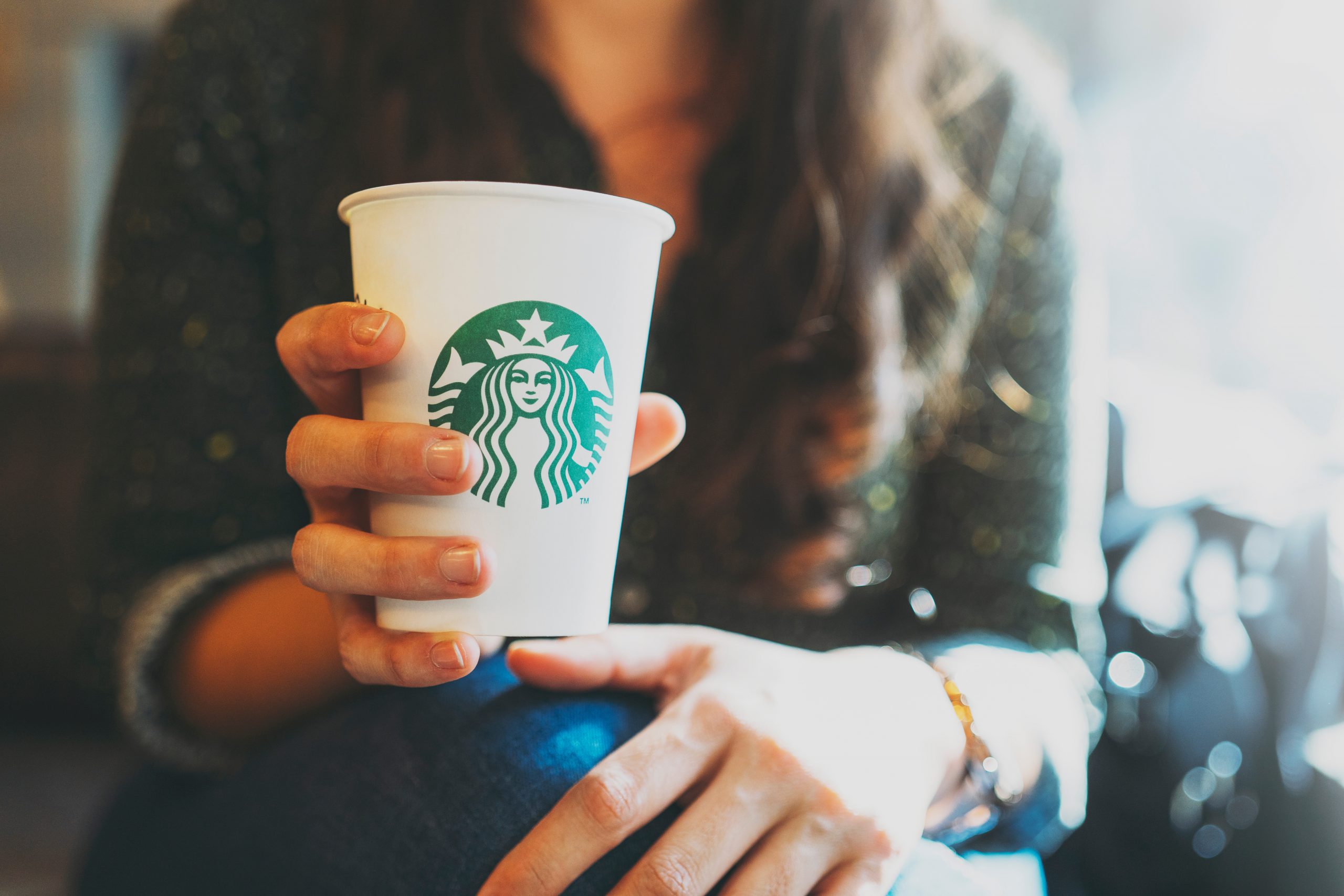 New York, USA - November 5, 2019 : Close up of a Woman drinking a tall Starbucks coffee in starbucks coffee shop with carrot cake.