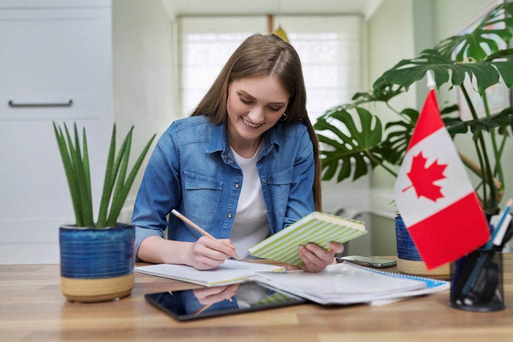 Online training, female teenager sitting at home looking at webcam, Canadian flag on table