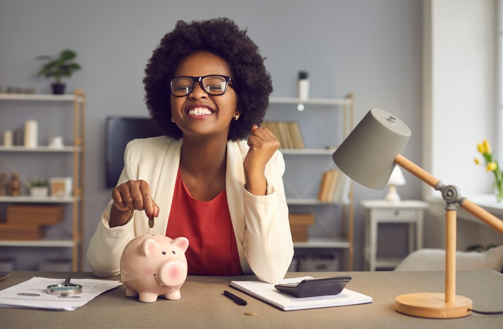 Excited happy african american woman with yes gesture putting coin in piggybank